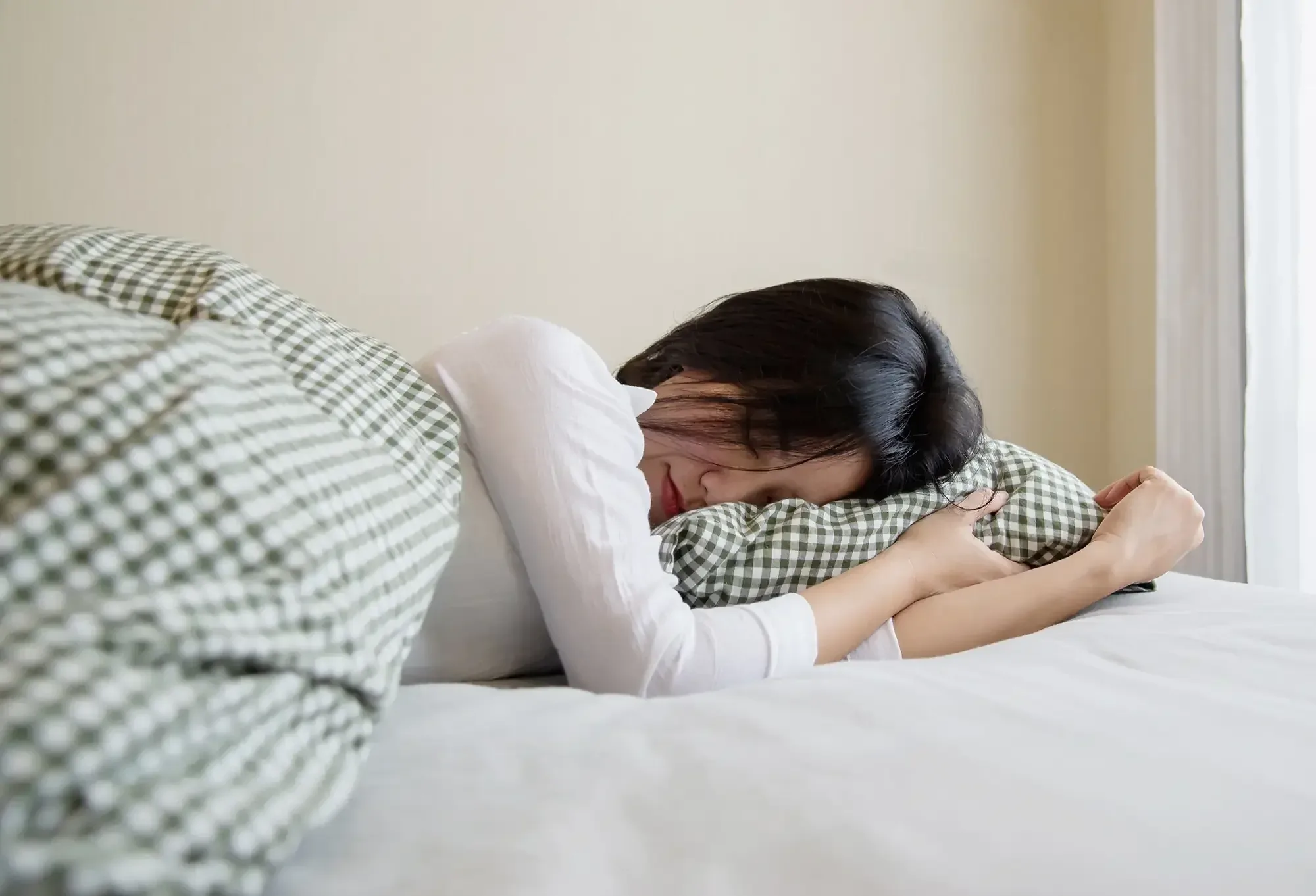 A woman asleep face down, smiling, hugging a green gingham pillow