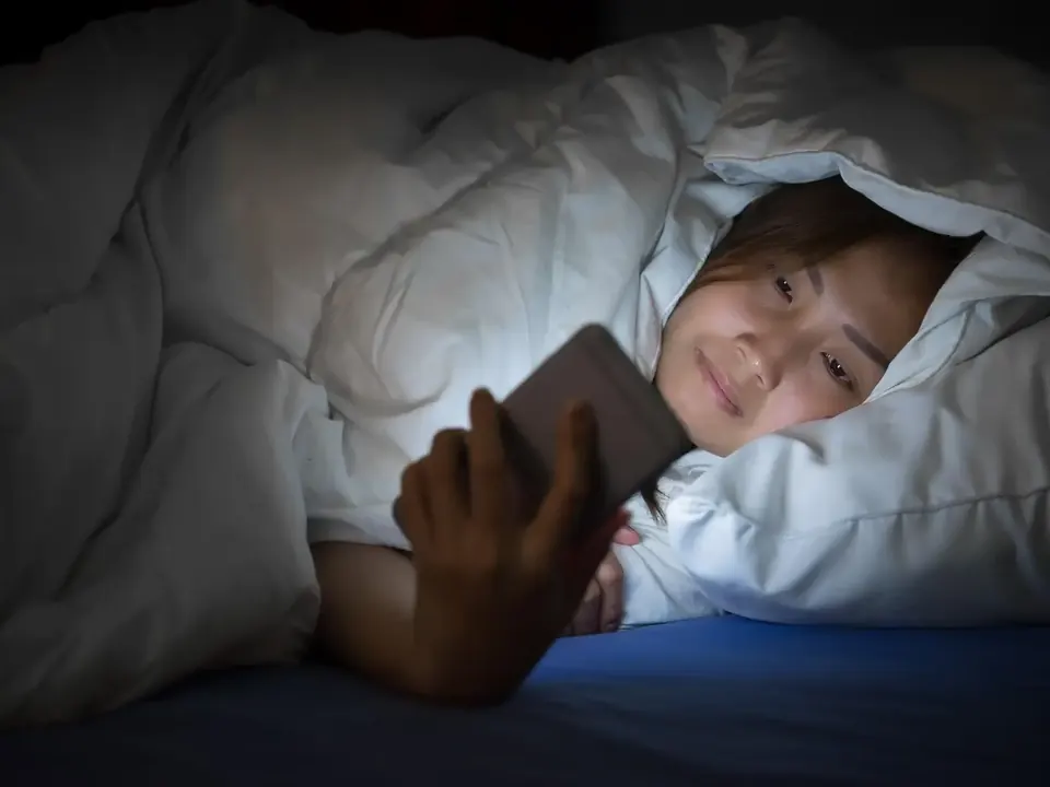 Woman scrolling her phone under the duvet late at night